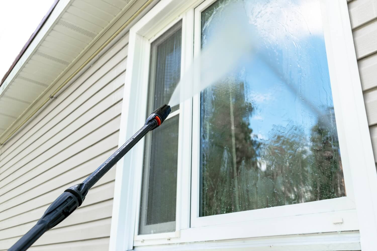 Pressure washing exterior siding around a window at an Odell home