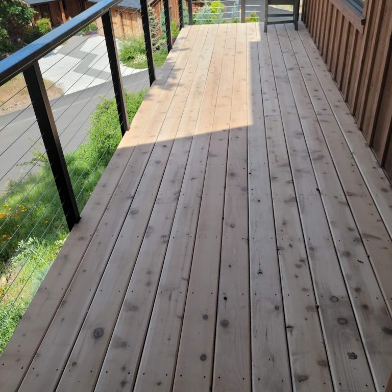 Painter brushing stain onto wood decking at an Odell, OR home